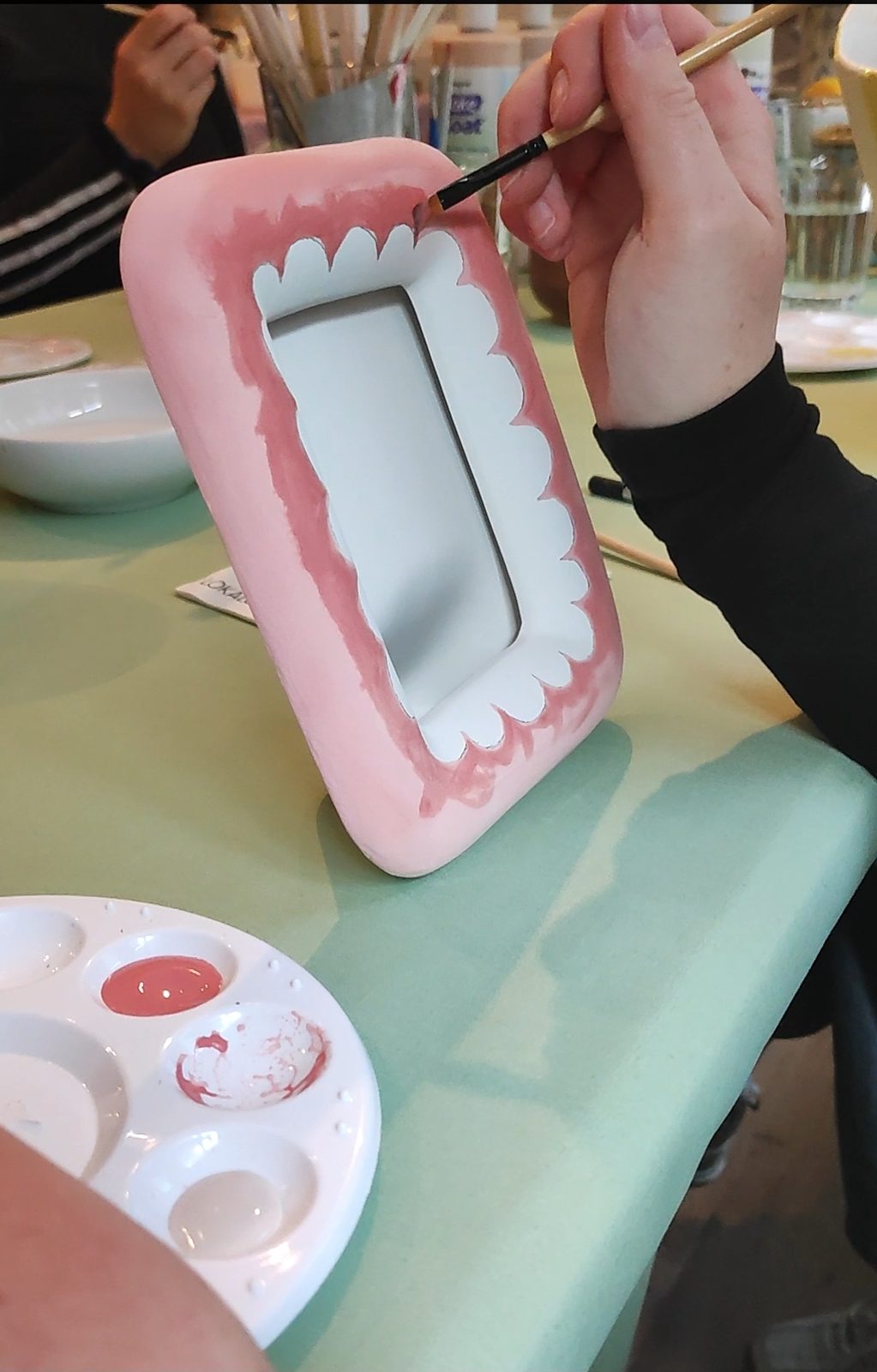 Ein rosa Keramik-Bilderrahmen wird mit dem Pinsel bemalt