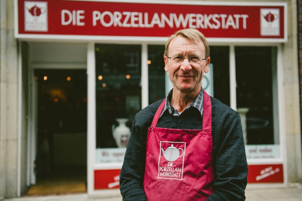 Harald Schmalhaus in roter Schürze vor dem Laden der Porzellanwerkstatt